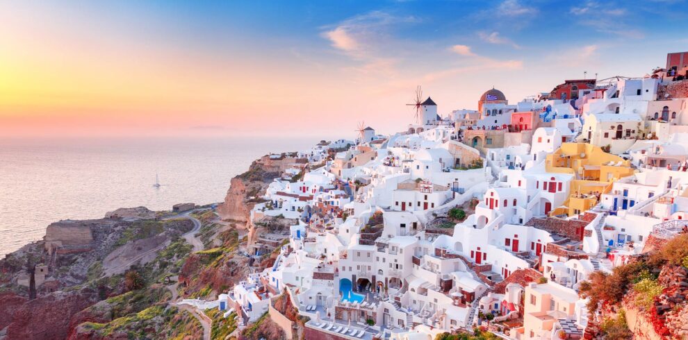 Iconic whitewashed houses and windmills of Oia in Santorini at sunset, overlooking the Aegean Sea.