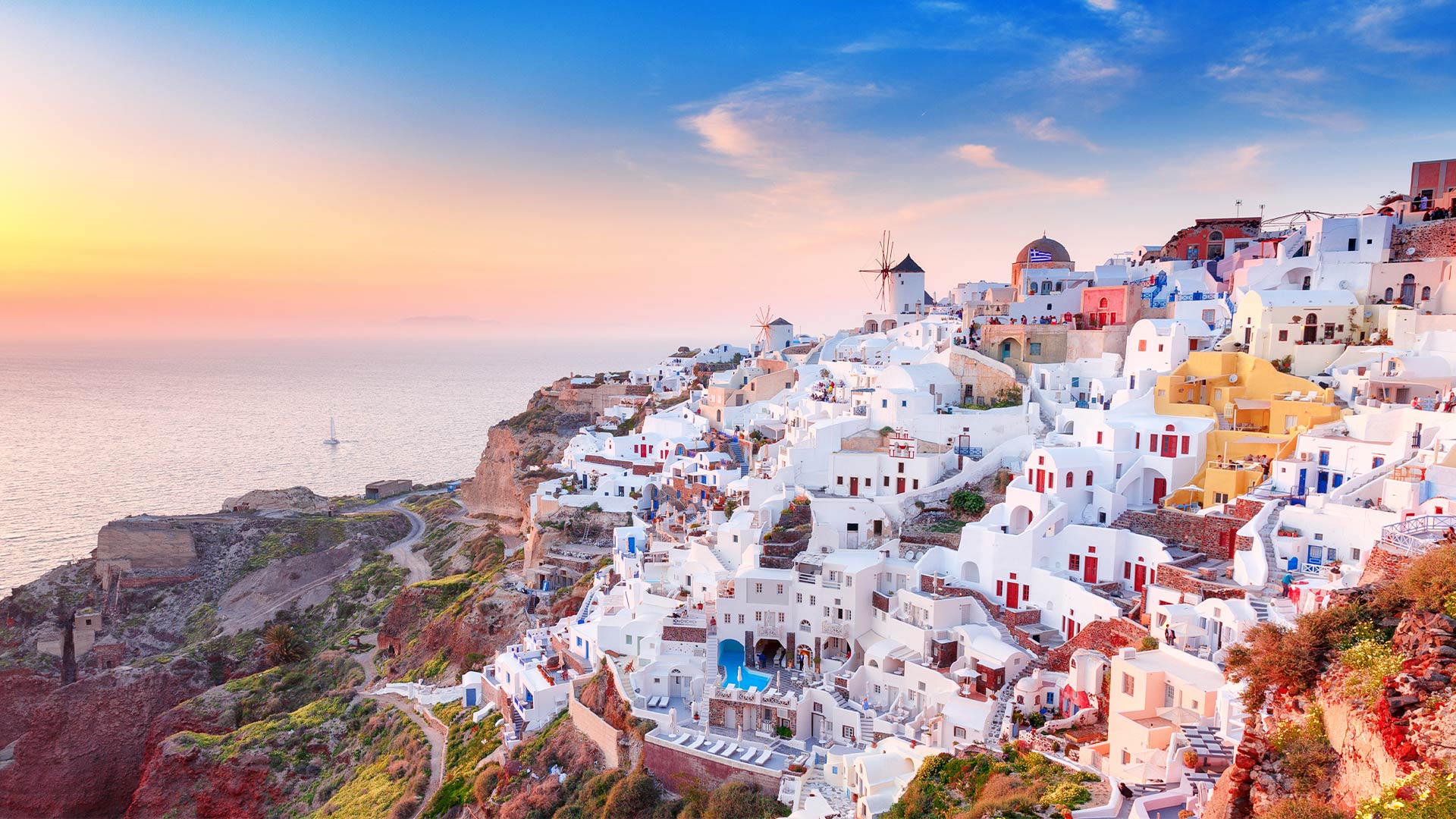 Iconic whitewashed houses and windmills of Oia in Santorini at sunset, overlooking the Aegean Sea.