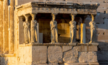 The Caryatids of the Erechtheion on the Acropolis of Athens, illuminated by golden sunlight at sunset.