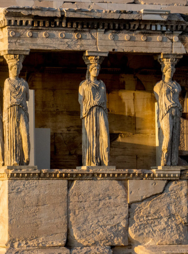 The Caryatids of the Erechtheion on the Acropolis of Athens, illuminated by golden sunlight at sunset.