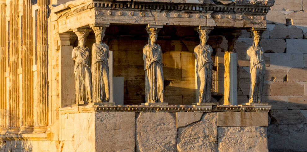 The Caryatids of the Erechtheion on the Acropolis of Athens, illuminated by golden sunlight at sunset.