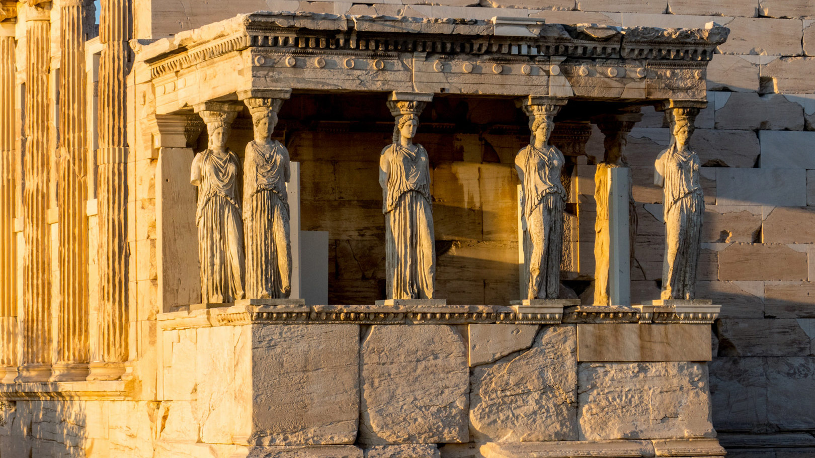 The Caryatids of the Erechtheion on the Acropolis of Athens, illuminated by golden sunlight at sunset.