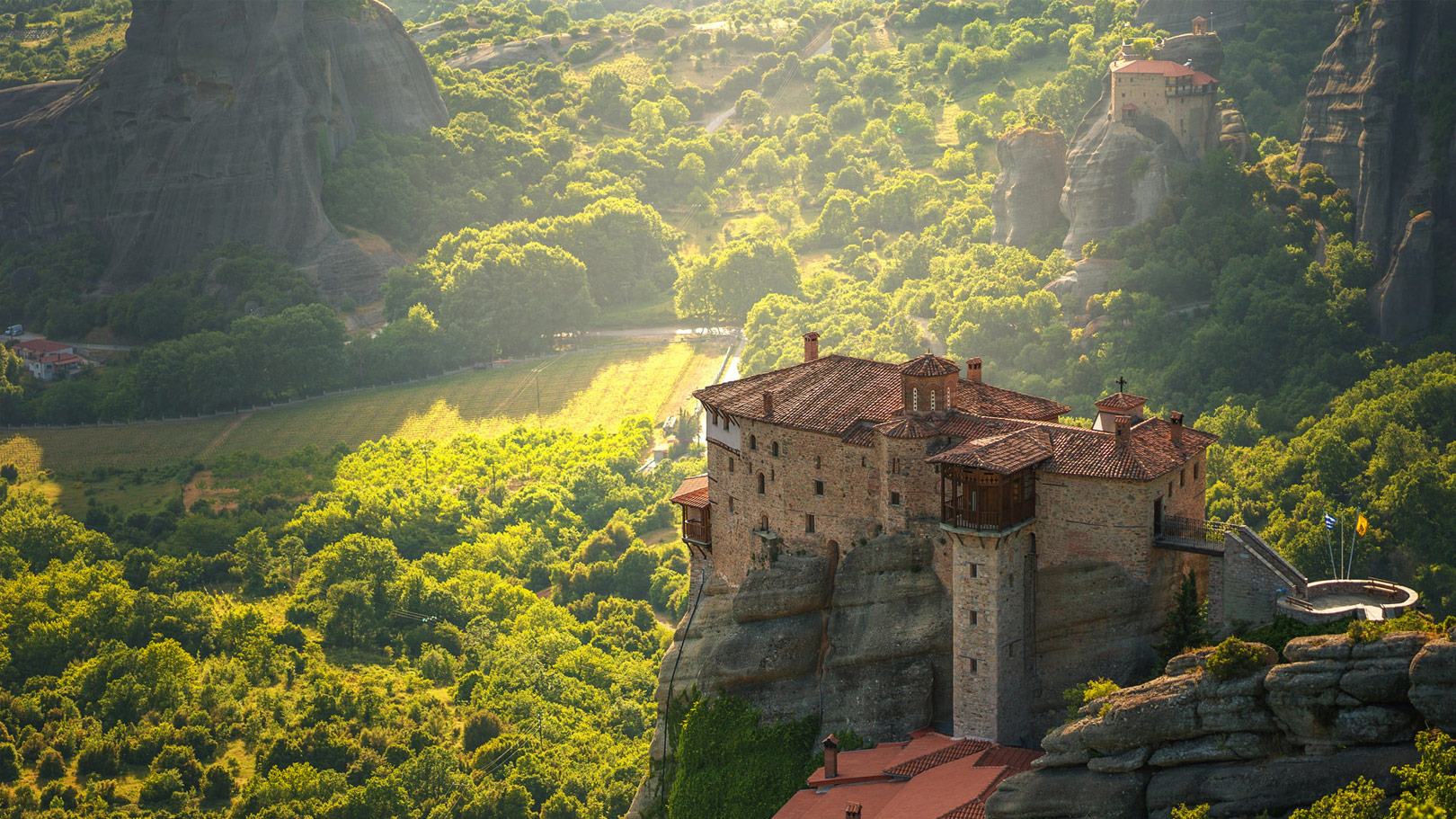 Monastery perched atop dramatic rock formations in Meteora, surrounded by lush green valleys and golden sunlight.