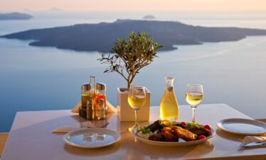 Traditional Greek meal with wine served on a terrace overlooking the caldera and sea views in Santorini at sunset.