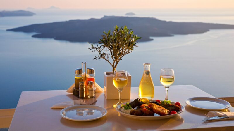 Traditional Greek meal with wine served on a terrace overlooking the caldera and sea views in Santorini at sunset.