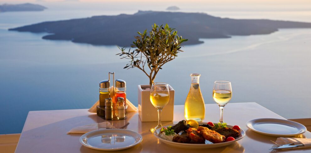 Traditional Greek meal with wine served on a terrace overlooking the caldera and sea views in Santorini at sunset.