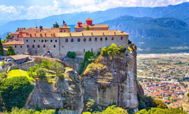 Monastery perched atop a rock formation in Meteora, Greece, surrounded by mountains, a highlight of a winter mainland tour.