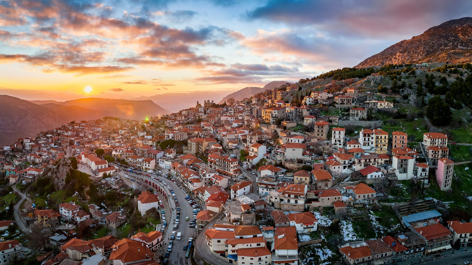 Aerial view of Arachova village in central Greece with red-roofed houses on a mountainside at sunset.
