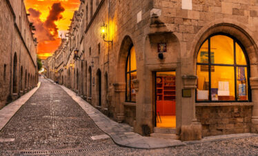 Sunset view of the medieval Street of the Knights in Rhodes Old Town with historic stone buildings and warm lights.
