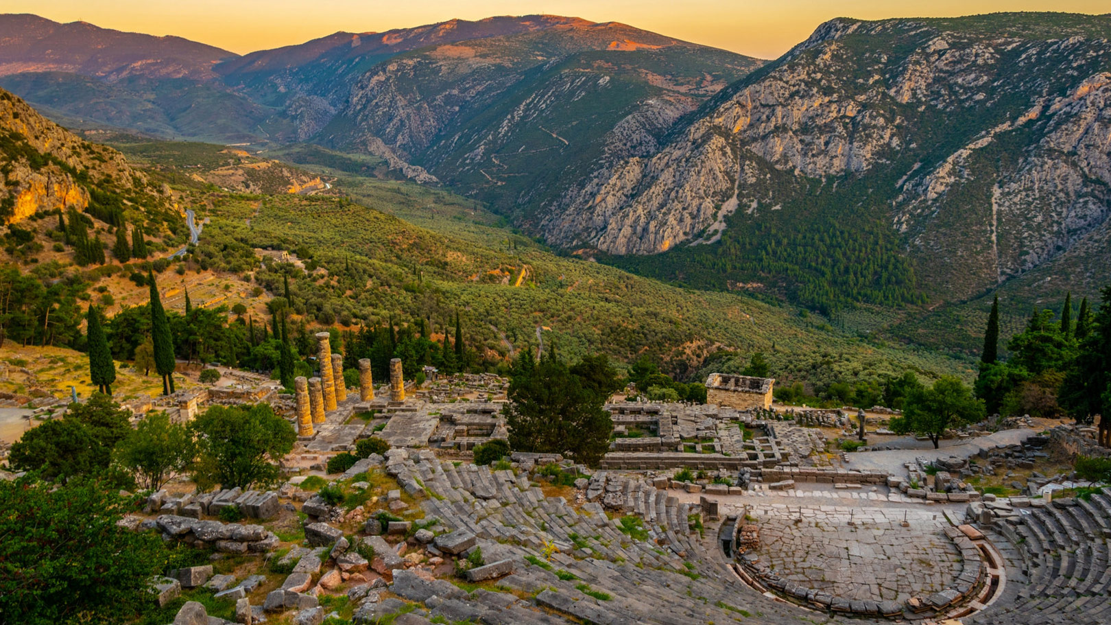 Ancient theatre and ruins of Delphi set against dramatic mountain scenery in central Greece at sunset.