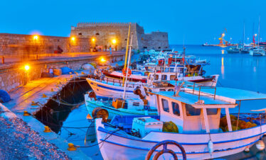 Traditional fishing boats docked in the illuminated harbor of Heraklion, Crete, with the Venetian fortress at dusk.