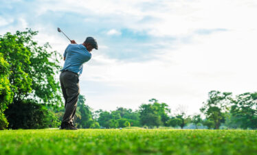Golfer swinging a club on a lush green course under a bright sky, capturing the essence of golfing in nature.