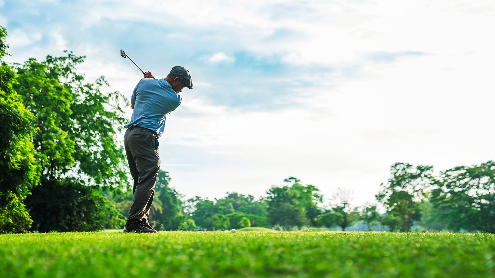 Golfer swinging a club on a lush green course under a bright sky, capturing the essence of golfing in nature.