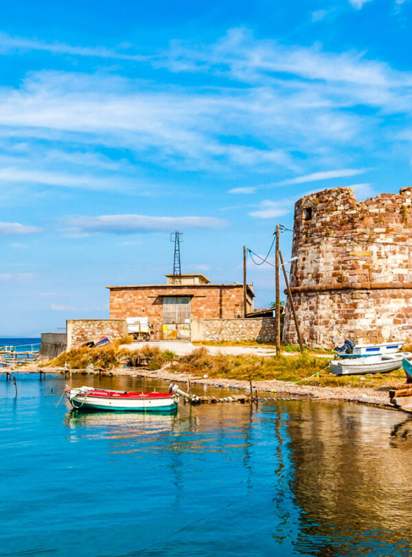 Scenic harbor with traditional fishing boats and a historic stone tower on the island of Lesvos, Greece.