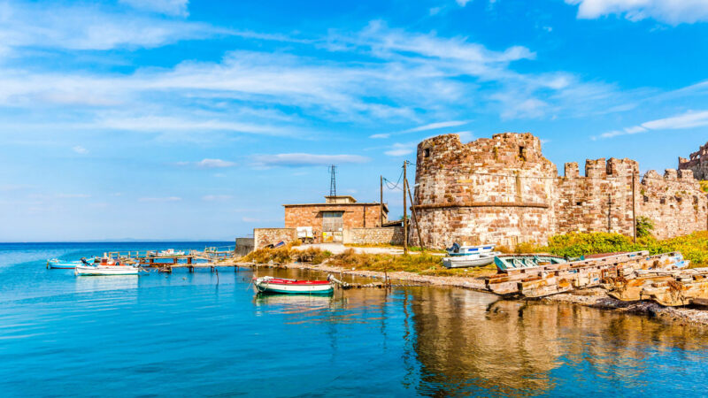 Scenic harbor with traditional fishing boats and a historic stone tower on the island of Lesvos, Greece.