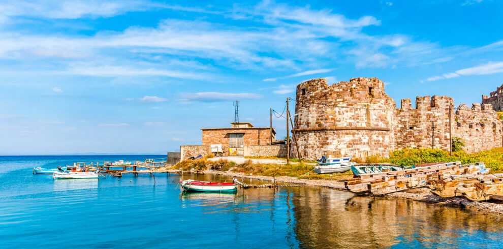 Scenic harbor with traditional fishing boats and a historic stone tower on the island of Lesvos, Greece.