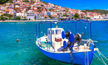 Traditional fishing boat floating on the blue waters of Lesvos with a colorful hillside village in the background.