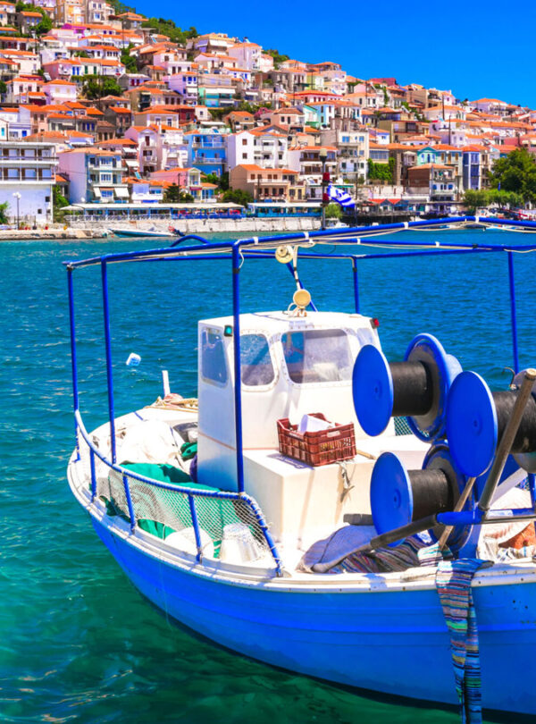 Traditional fishing boat floating on the blue waters of Lesvos with a colorful hillside village in the background.
