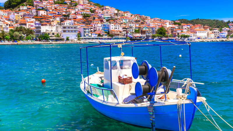 Traditional fishing boat floating on the blue waters of Lesvos with a colorful hillside village in the background.