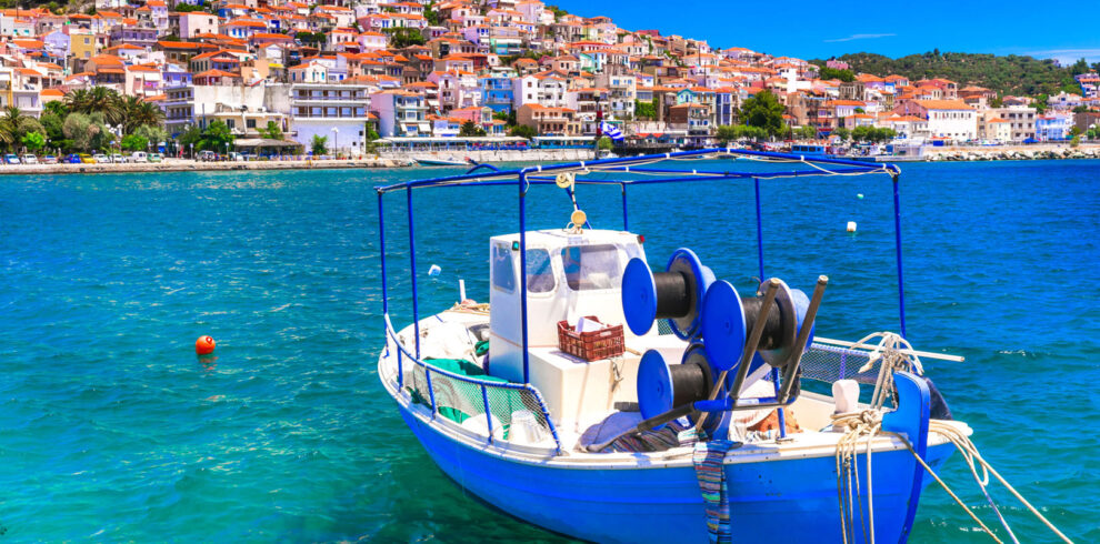 Traditional fishing boat floating on the blue waters of Lesvos with a colorful hillside village in the background.