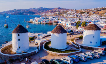Iconic windmills overlooking the Aegean Sea and whitewashed houses of Mykonos Town on a sunny day.