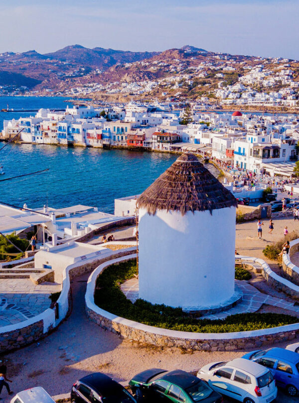 Iconic windmills overlooking the Aegean Sea and whitewashed houses of Mykonos Town on a sunny day.