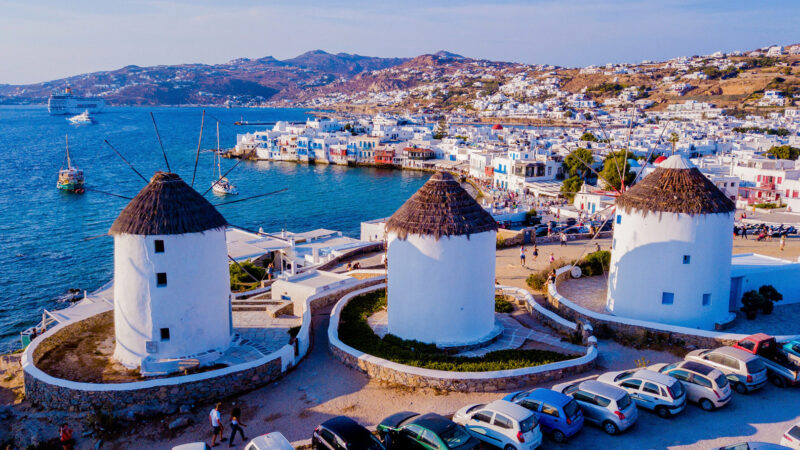 Iconic windmills overlooking the Aegean Sea and whitewashed houses of Mykonos Town on a sunny day.