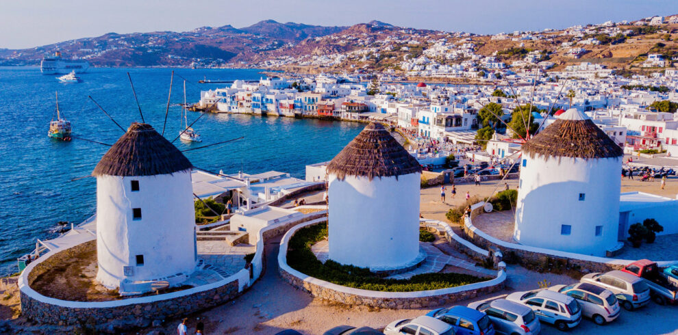 Iconic windmills overlooking the Aegean Sea and whitewashed houses of Mykonos Town on a sunny day.