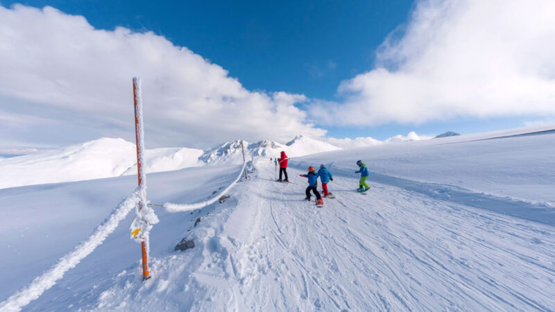 Skiers on a snowy mountain slope under a bright blue sky, enjoying winter sports in a Greek ski resort.