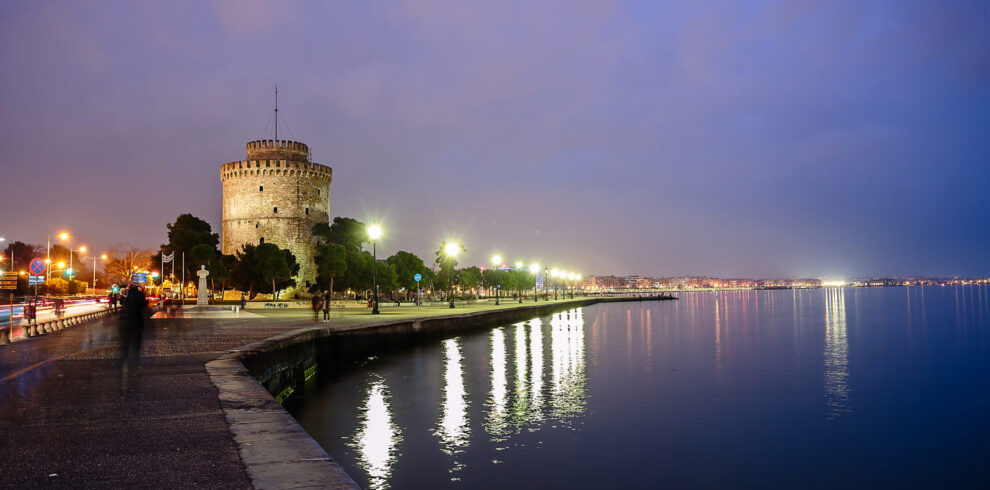 Twilight view of Thessaloniki’s White Tower and waterfront promenade reflected in the calm waters of the Thermaic Gulf.