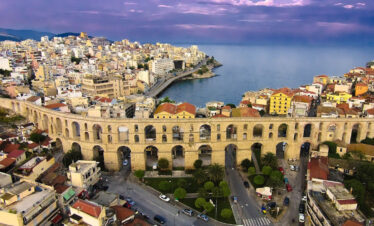 Aerial view of the historic Kamares aqueduct in Kavala with the city’s coastal skyline and the Aegean Sea beyond.