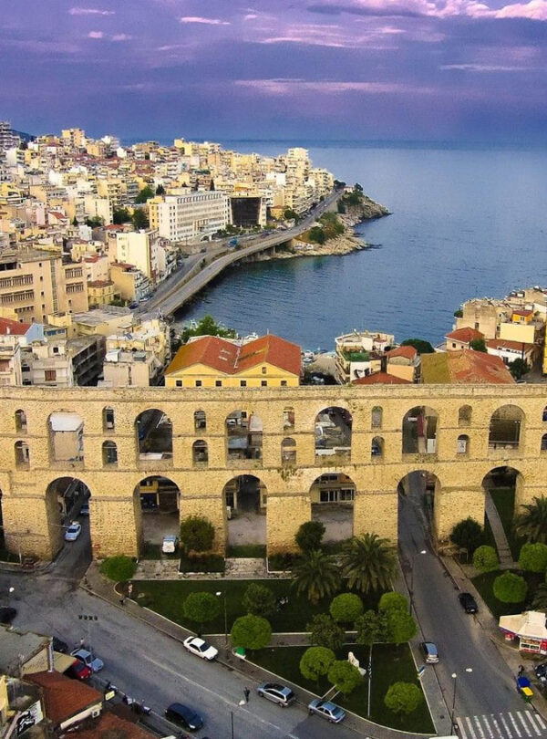 Aerial view of the historic Kamares aqueduct in Kavala with the city’s coastal skyline and the Aegean Sea beyond.