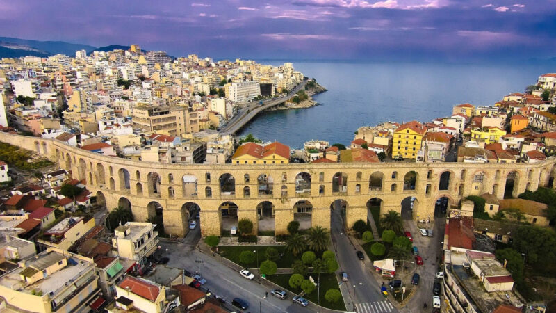 Aerial view of the historic Kamares aqueduct in Kavala with the city’s coastal skyline and the Aegean Sea beyond.