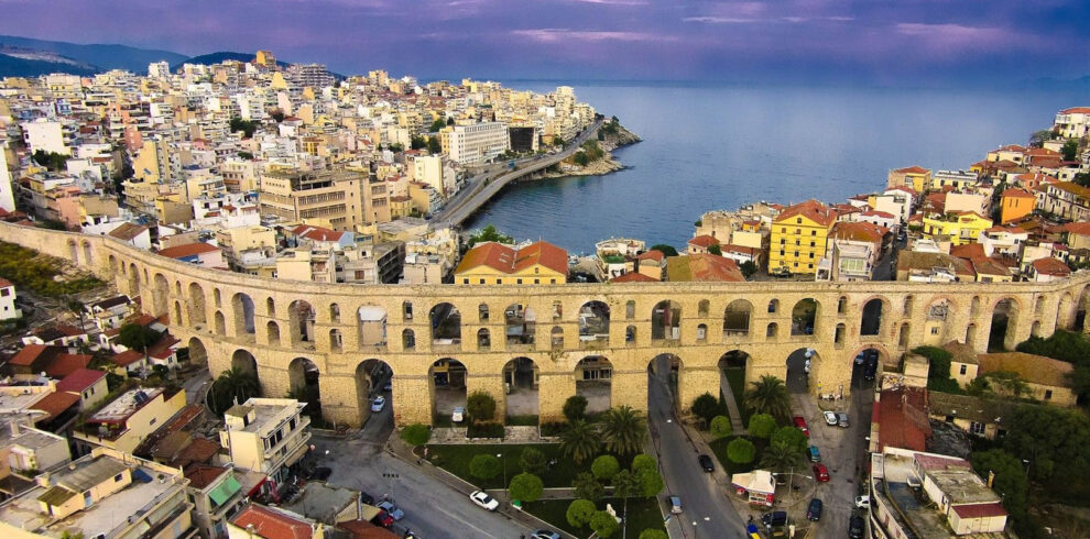 Aerial view of the historic Kamares aqueduct in Kavala with the city’s coastal skyline and the Aegean Sea beyond.