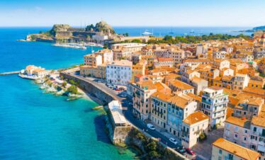 Aerial view of Corfu’s old town with colorful Venetian buildings, coastal walls, and the Ionian Sea in the background.