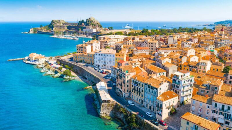 Aerial view of Corfu’s old town with colorful Venetian buildings, coastal walls, and the Ionian Sea in the background.
