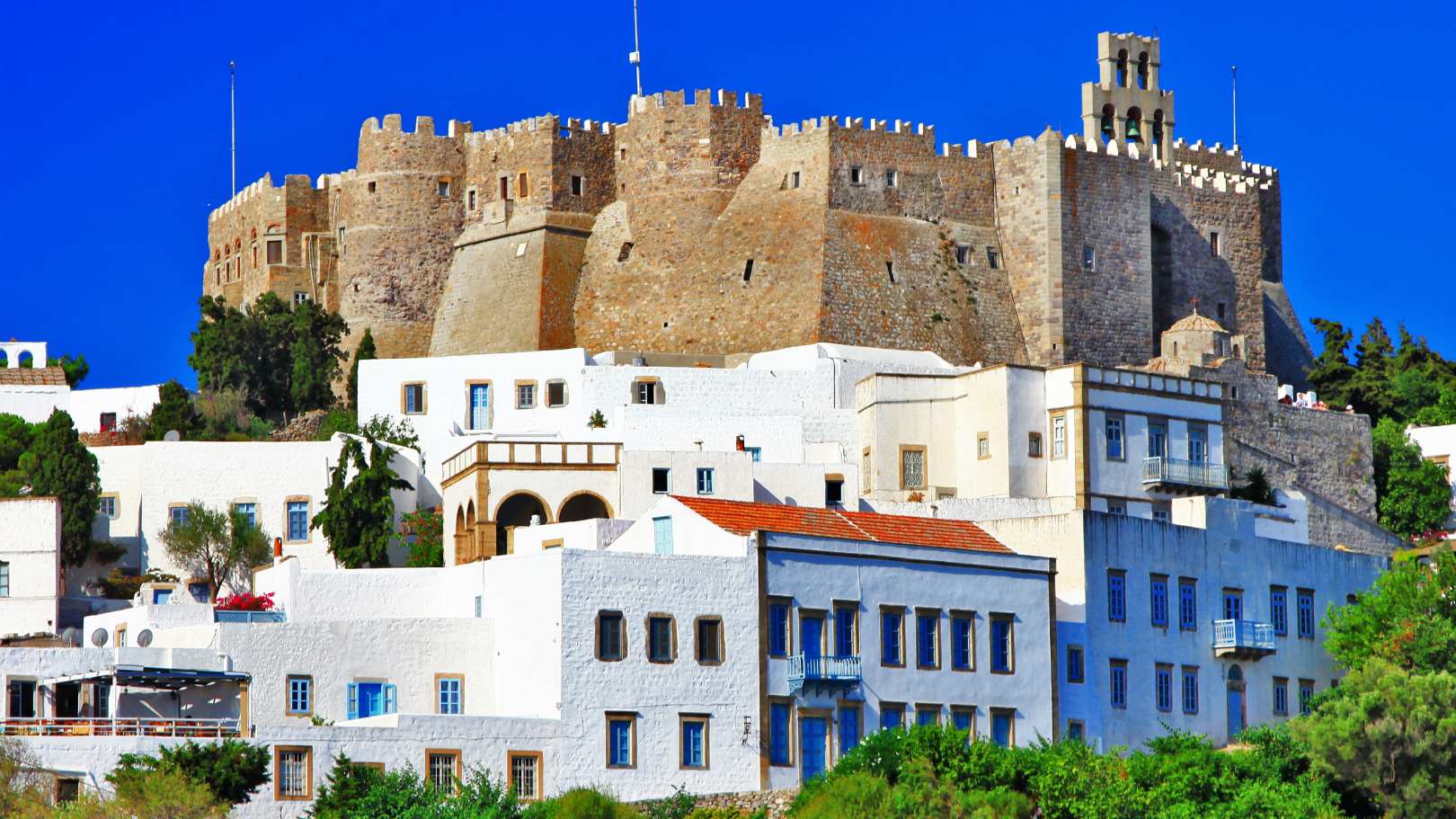 The imposing Monastery of Saint John the Theologian towers above the whitewashed houses of Chora in Patmos, Greece, under a vibrant blue sky.