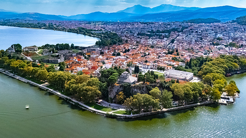 Aerial view of Ioannina’s historic old town and lakefront fortress surrounded by Pamvotida Lake and mountains.