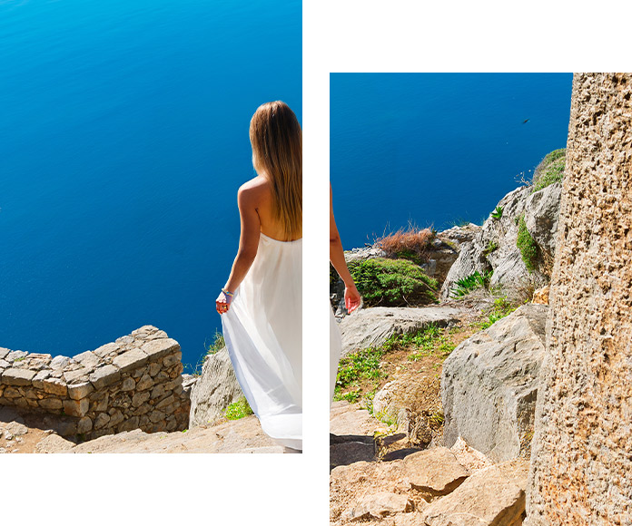 Woman in a white dress descending stone steps toward the deep blue Aegean Sea, symbolizing dream travel experiences.