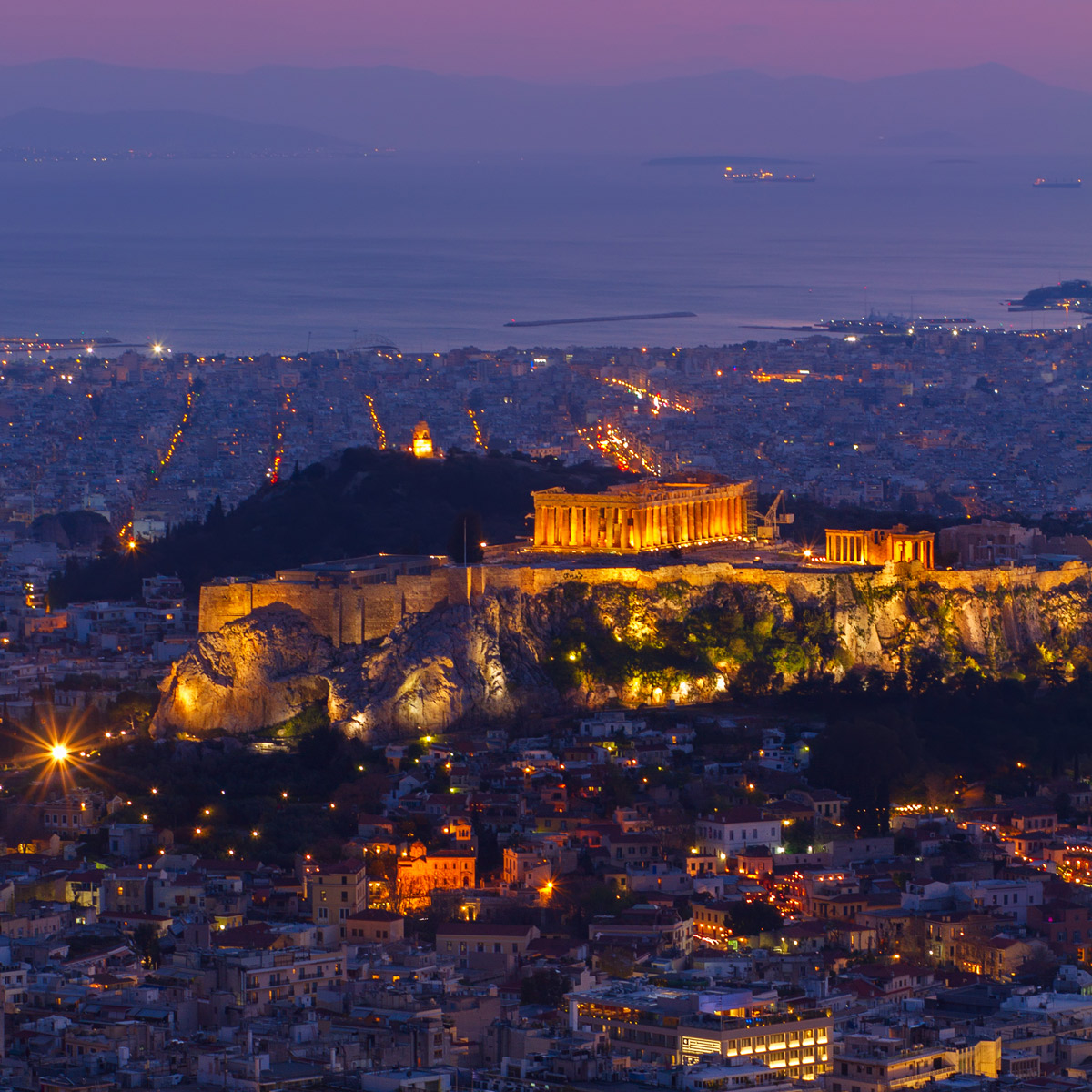 The Acropolis and the Parthenon lit up at dusk above Athens